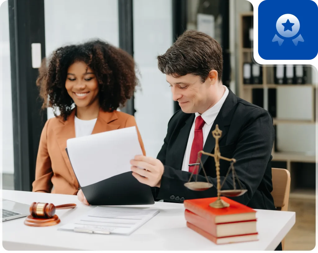 A lawyer reviews documents with a client at a table featuring a scale of justice and legal books in an office setting.
