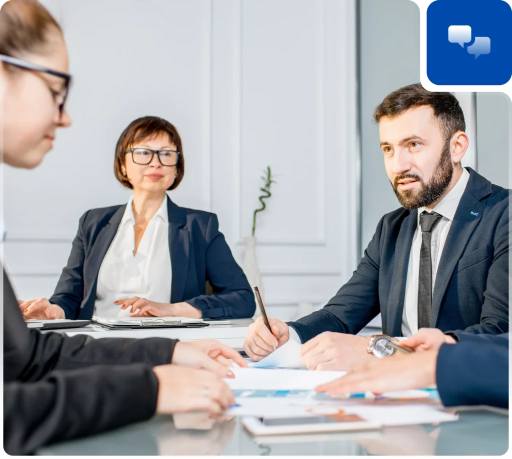 A group of professionals in business attire engaged in a meeting around a conference table with documents and notes.