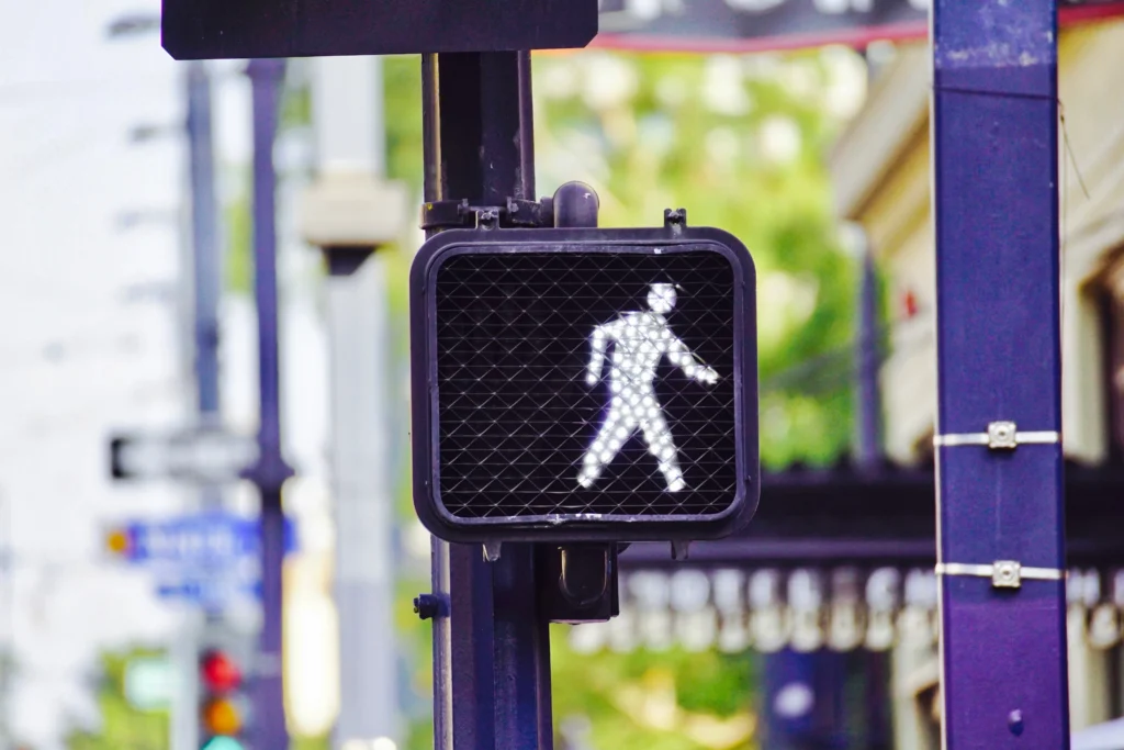 A glowing pedestrian walk signal shows a silhouetted figure walking, mounted on a street pole against a blurred urban backdrop.