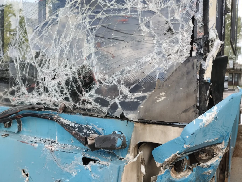 Close-up of a damaged blue vehicle, featuring a severely cracked windshield and dented bodywork from an apparent collision.