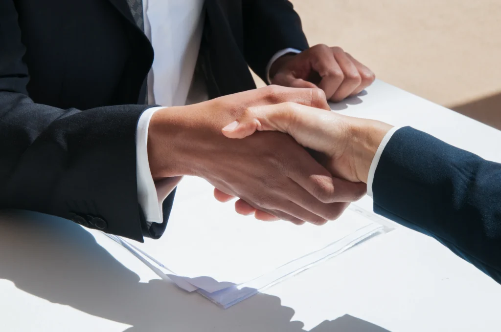 Two people in business attire shake hands over a table with papers, symbolizing a professional agreement or partnership.